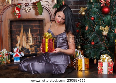 Happy romantic  woman sitting under Christmas tree with pile of Christmas presents