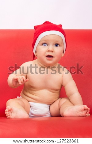 Little cute boy dressed in santa clause hood sitting on sofa