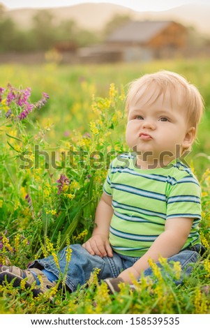 funny brown-eyed boy sitting in a field of flowers on the background of the house