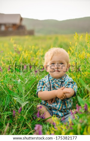 funny boy sitting in a field of flowers on the background of the house