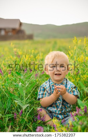 funny boy sitting in a field of flowers on the background of the house