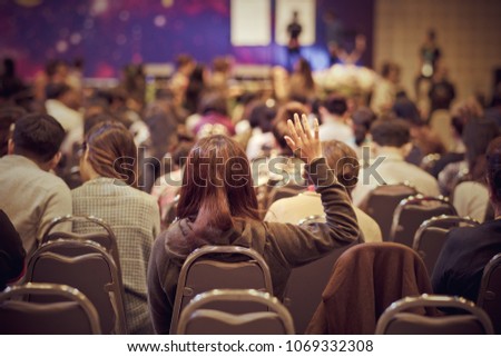 Speaker on the stage with Rear view of Audience in put hand up acton for question in the meeting or seminar meeting, business and education concept