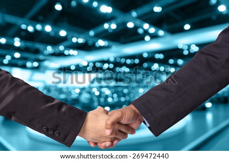 Hand shake between a businessman and a businesswoman on abstract blurred photo of motor show background