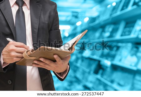 Businessman writing the note book on Abstract blurred photo of book store background, blur color tone