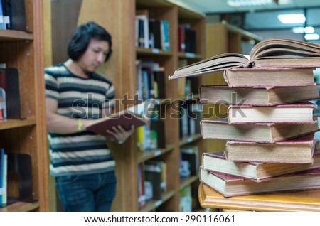stack of old book on the desk in library with the man reading over the book blur background