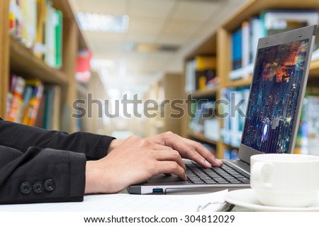 Businessman using the laptop with coffee cup on the Abstract blurred photo of library background