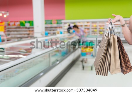 Holding shoping bags by hand on Supermarket with Abstract blurred photo of store with trolley in department store bokeh background