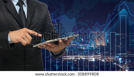 businessman using the tablet on Trading graph on the cityscape at night and world map background,Business financial concept