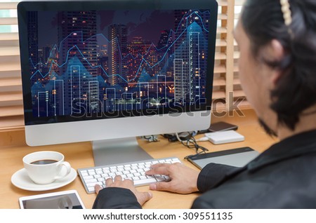 Rear view of a businessman working with a computer and tablet of business trading graphat screen on the office desk