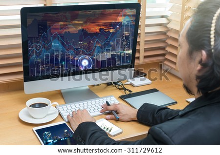 Rear view of a businessman working with a computer and tablet of business trading graph at screen on the office desk