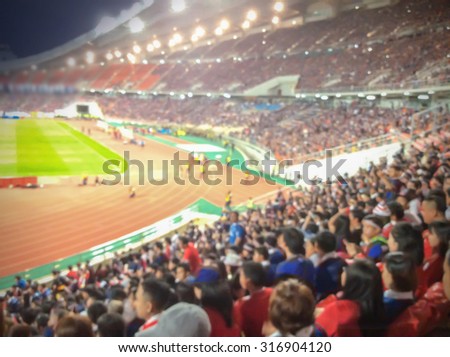 Abstract blurred photo crowd of spectators on a stadium with a football match, sport background concept
