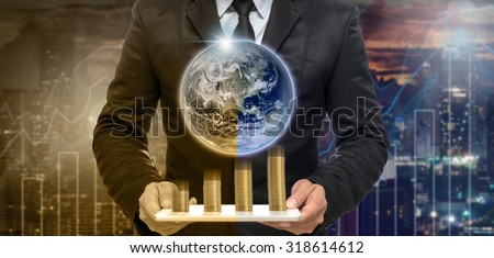 Businessman holding the tablet with earth and stack of golden coins on Trading graph on the cityscape at night and world map background,Elements of this image furnished by NASA