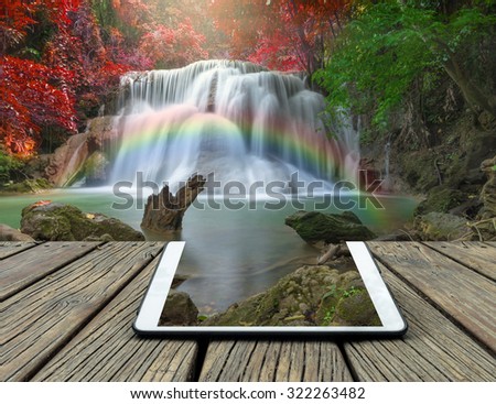 Conceptual image of a tablet on Beautiful waterfall with soft focus and rainbow in the forest