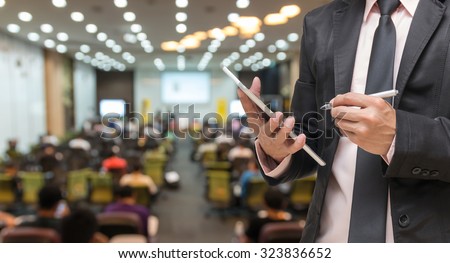 Businessman using the tablet on the Abstract blurred photo of conference hall or seminar room with attendee background