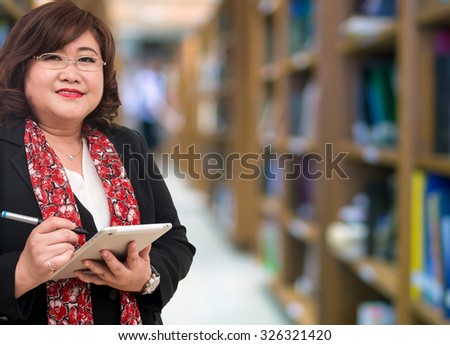 Professor Senior woman using the tablet on the library blurred background, education concept