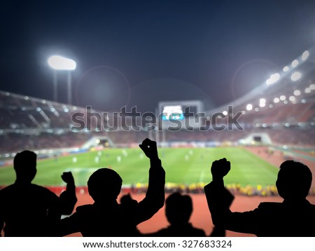 Silhouettes of football fans cheering against large football stadium with lights, sport concept