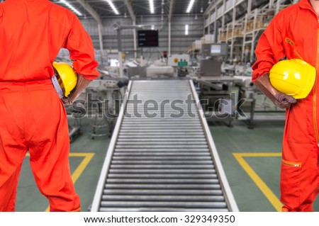 Asian engineers worker holding a yellow hardhat on Factory conveyor line transporting package blurred background, industrial concept