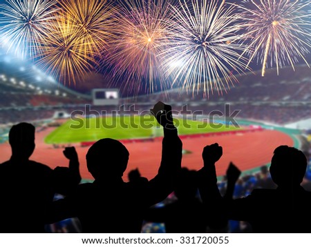 Silhouettes of football fans cheering against large football stadium with colorful fireworks, sport concept