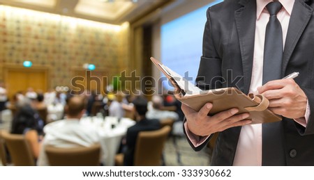 Businessman writing the note book on the Abstract blurred photo of conference hall or seminar room with attendee background