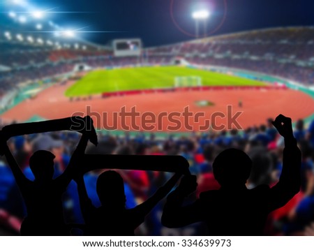 Silhouettes of football fans cheering against large football stadium with lights, sport concept