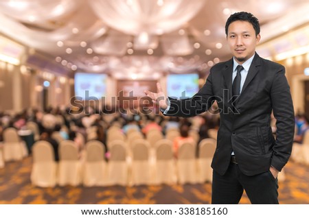 Asian Businessman with welcoming gesture on Abstract blurred photo of conference hall or seminar room with attendee background