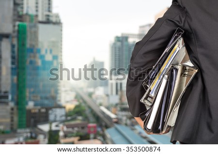 Businessman is holding many document folders on abstract Blurred photo of sky train with cityscape background, back side, business busy concept