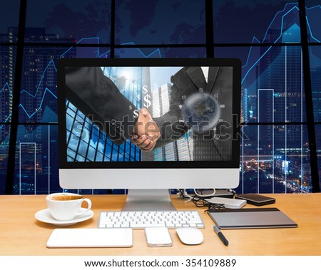 Workspace with computer desktop with Hand shake between businessman at the screen on the trading graph over the blurred photo of cityscape background,Elements of this image furnished by NASA