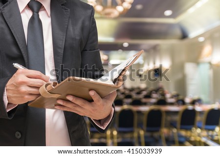 Businessman writing the note book on the Abstract blurred photo of conference hall or seminar room background