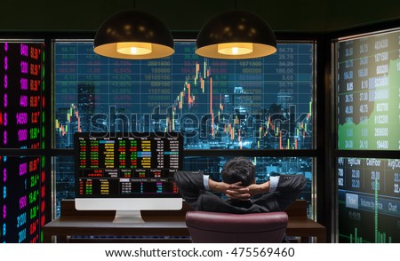 Back side of sitting businessman who is looking at big screen and desktop computer showing the trading graph of stock market exchange graph background, Business trading and finance concept