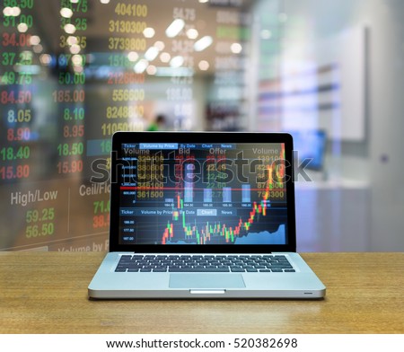 Stock exchange market trading graph over the screen of computer laptop on wood table over the photo blurred of trading graph background, business marketing trade concept