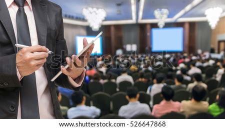 Businessman using the tablet on the Abstract blurred photo of conference hall or seminar room with attendee background, Business meeting concept