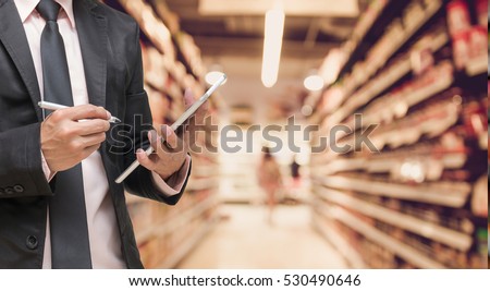 Businessman using the tablet and writing the order stock on Supermarket blur background, business technology concept