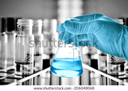 Flask in scientist hand with test tubes in rack background