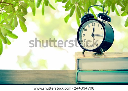 Retro alarm clock on text book with natural light and green leaf background