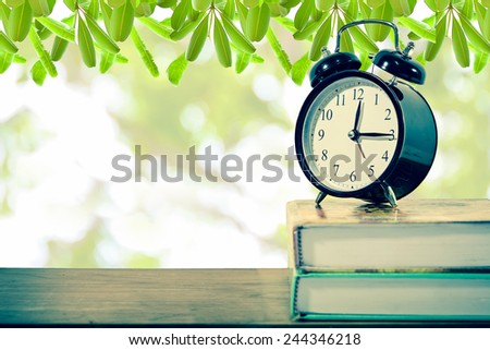 Retro alarm clock on text book with natural light and green leaf background