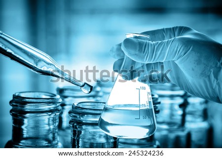 Flask in scientist hand with dropping chemical liquid to test tube