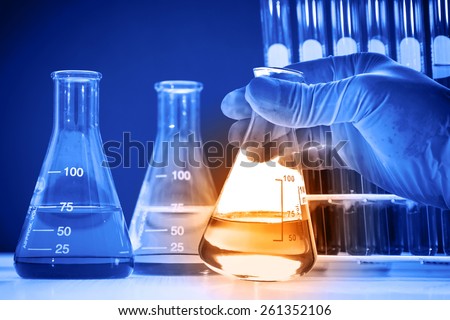 Flask in scientist hand with lab glassware background