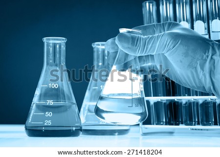 Conical flask in scientist hand with lab glassware background, blue tone