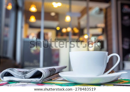 Cup of cappuccino with newspaper on the table, blur coffee shop background