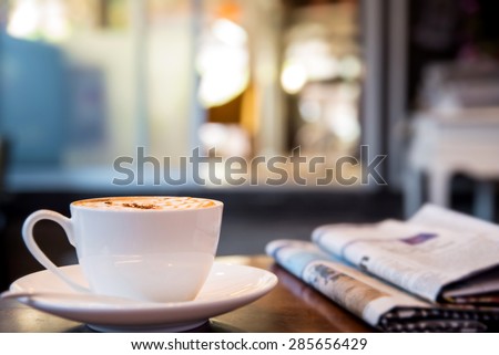 Cup of cappuccino with newspaper on the table, coffee shop background