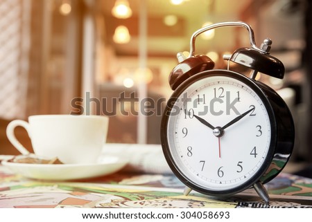 Retro alarm clock with cup of cappuccino and newspaper in coffee shop, coffee break time, warm tone