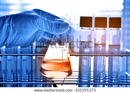 Flask in scientist hand with test tubes, laboratory research concept