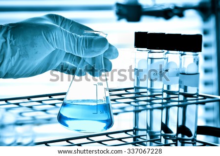 Flask in scientist hand with test tubes in laboratory