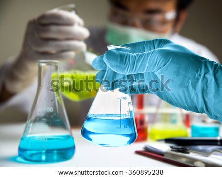 Flask in scientist hand with blur scientist in laboratory