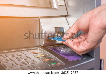 Hand inserting ATM card into bank machine to withdraw money