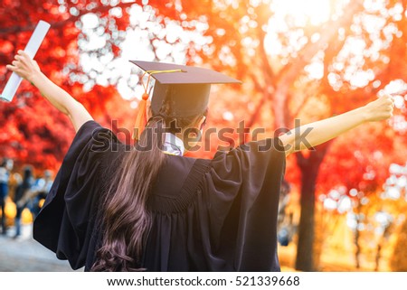 Graduate woman students wearing graduation hat and gown, autumn trees background