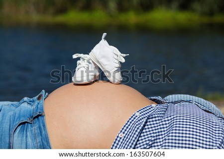 A pair of white shoes are placed on a pregnant mother belly