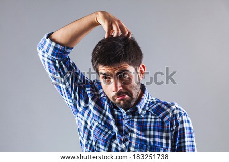 Young funny man is taking a decision while scratching his head as a monkey - isolated on grey