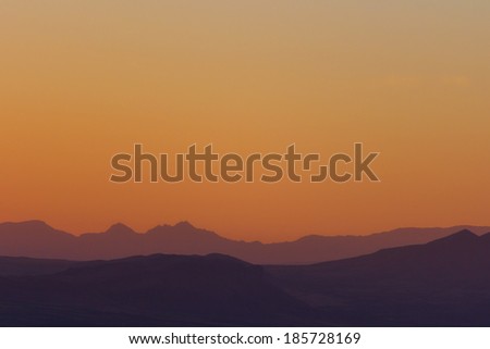 Hills and mountains silhouettes against orange sky at dusk