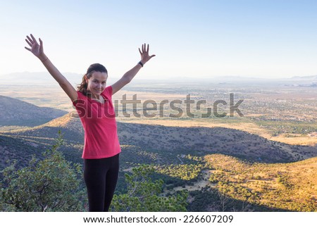 A girl holding hands in the air, on the top of a hill.